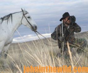 A hunter scouts out the area with binoculars while holding his horse's reins