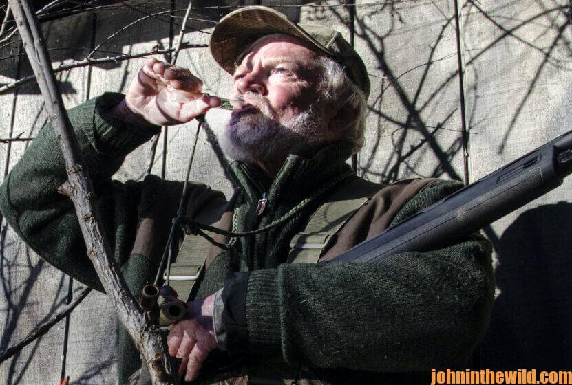 A hunter using a duck call outside his blind