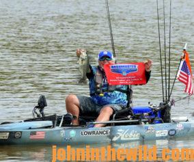 McElroy holds a bass and displays a tournament flag from his kayak