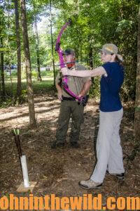 An instructor observes a bowhunting student taking aim with her bow