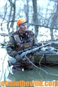 A hunter wading in a creek with his rifle in hand