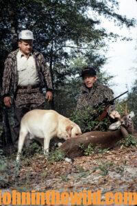 Two hunters and a dog retrieve a downed deer