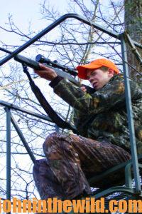 A hunter looking through his rifle scope in a tree stand