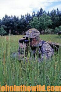A hunter looks over some tall grass with his binoculars