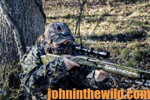 A hunter waits with aimed rifle for a turkey