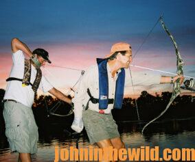 Two bowfishermen aim bows and arrows